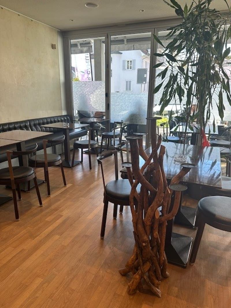 Wooden floor, black leather couches, tables and chairs, large windows, potted plant