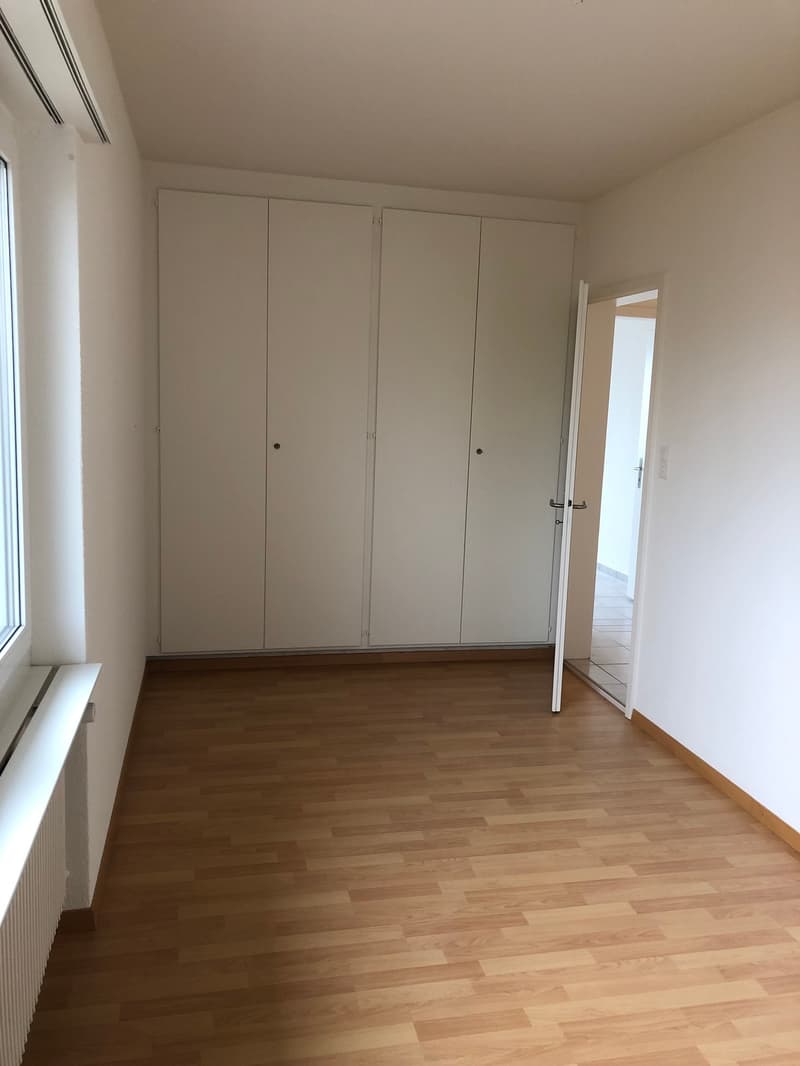 Spacious bedroom with white walls, hardwood flooring, and built-in closets along the wall.