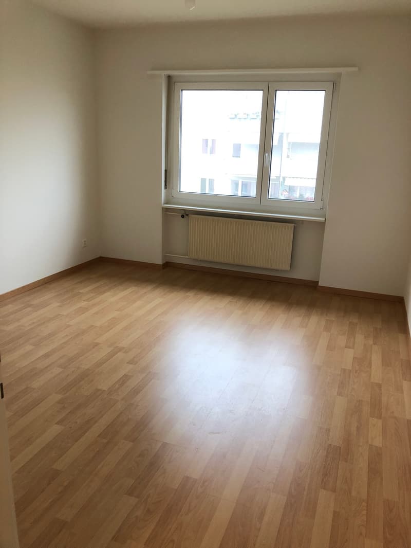 Empty room, large windows, wooden floors, white walls, heating radiator
