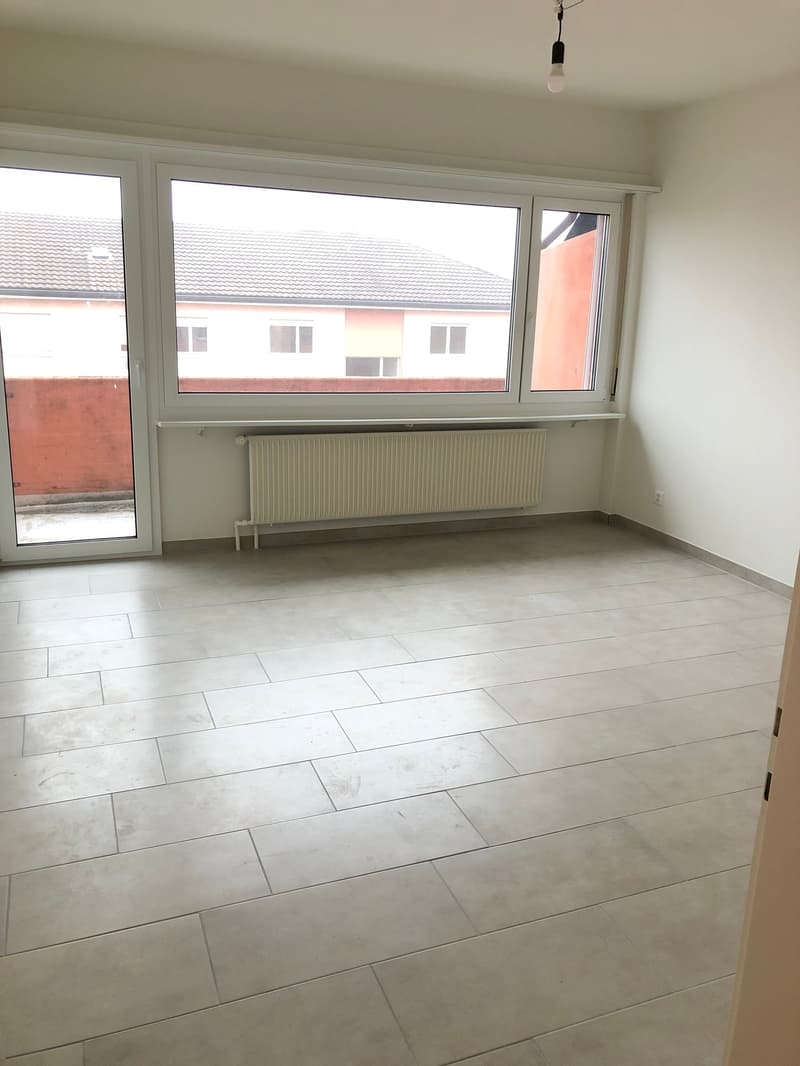 Empty room with white tiles, large windows, radiator, sliding door