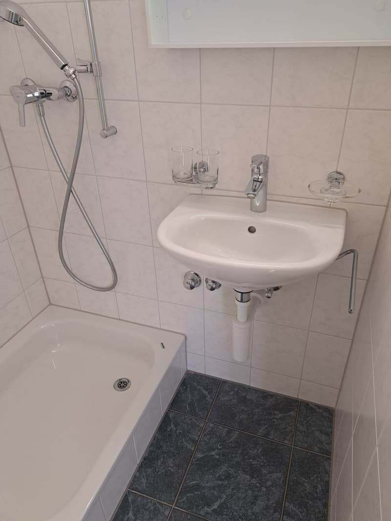 modern bathroom with a bathtub, white tiled walls, a sink, a faucet, and a mirror above the sink.