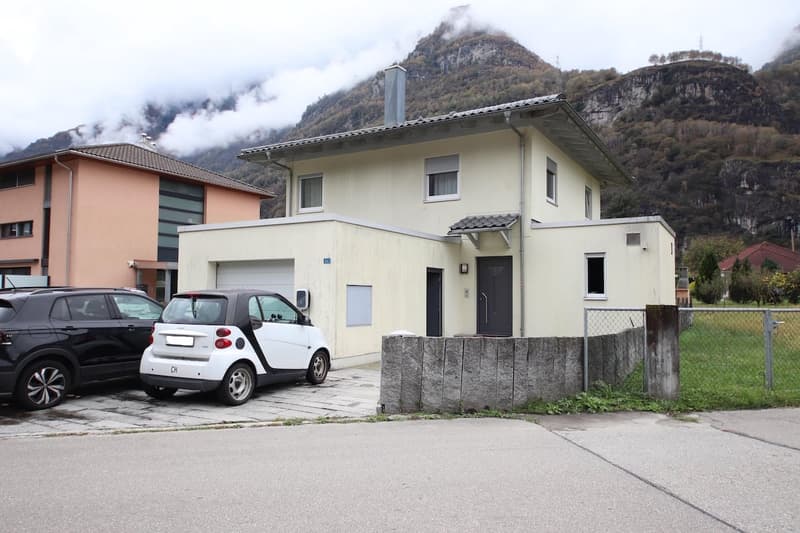 Two story house, white walls, grey roof, garage, large mountain range behind