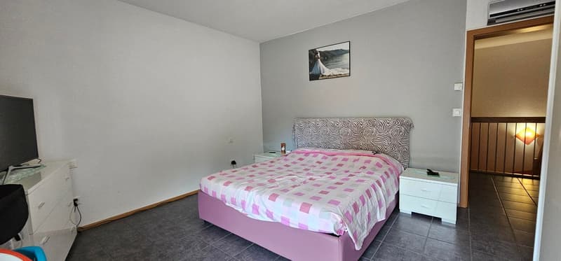 Spacious bedroom with gray walls, large bed with patterned bedding, dresser, and a framed artwork on the wall