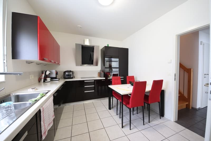 modern kitchen, black cabinets, red chairs, white tiled floor, stainless steel sink, wooden door, open entrance to another room