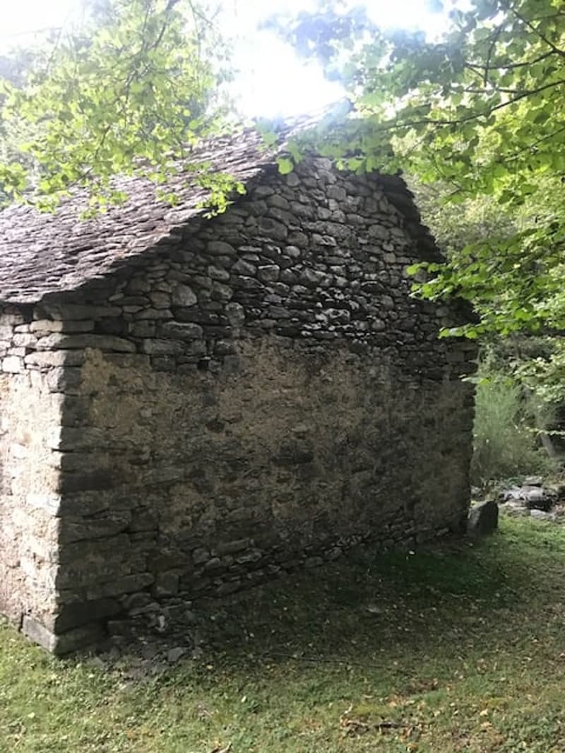Old stone building with a slate roof, surrounded by lush greenery and trees