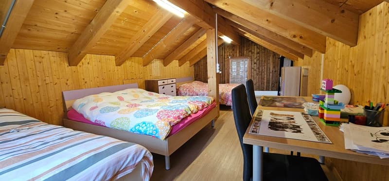 A room with wooden walls and beams, three beds, a table, and some toys