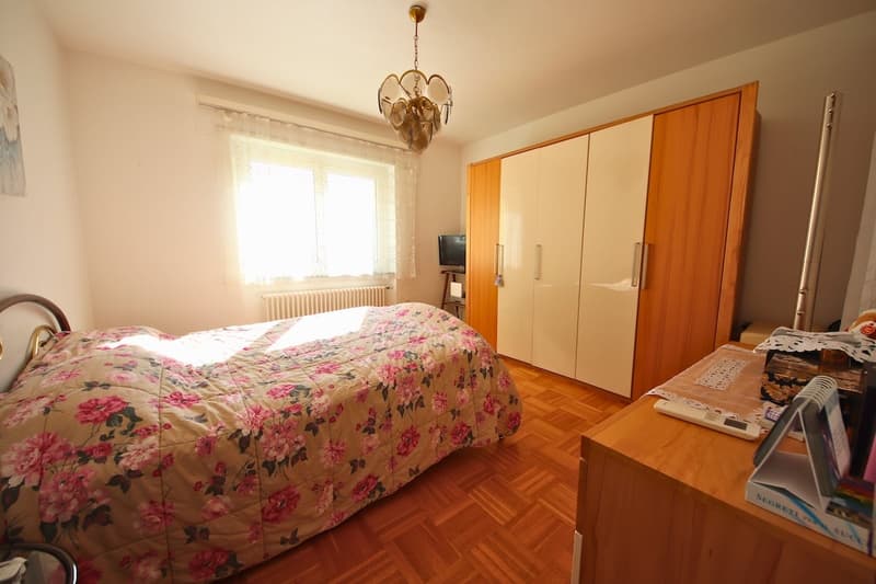 large double bed, bedspread, wardrobe, chandelier, TV, desk, books, radiator, window with curtains