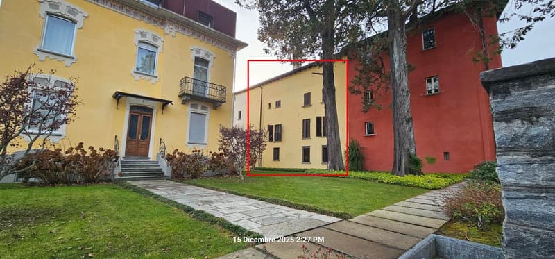 Front of the building with balcony, yellow painted exterior, steps leading up to the entrance, lawn in front.
