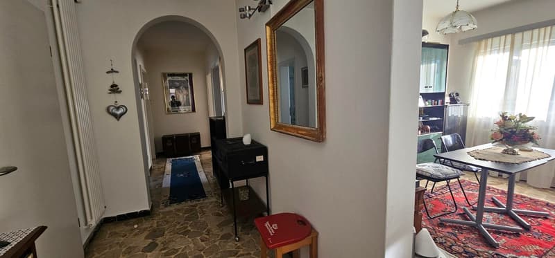 tiled flooring, arched doorway, framed paintings, large mirror, rug, desk with flowers, chairs