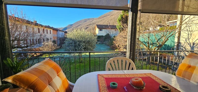 Balcony with a table and chairs, mountain view, iron railing, two pillows, small table with objects on it