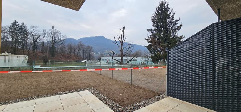 Outdoor patio with tiled flooring, surrounded by gravel, surrounded by a chain link fence, with a view of a mountainous landscape