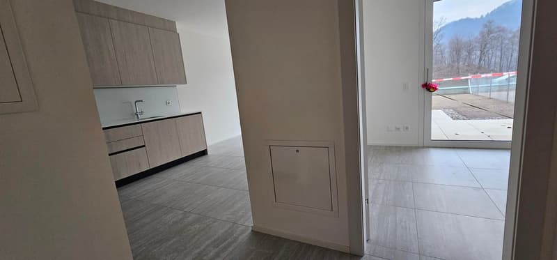 Empty kitchen with tiled floor, wall cabinets, countertop, sink, faucet, and large glass door leading to balcony with view