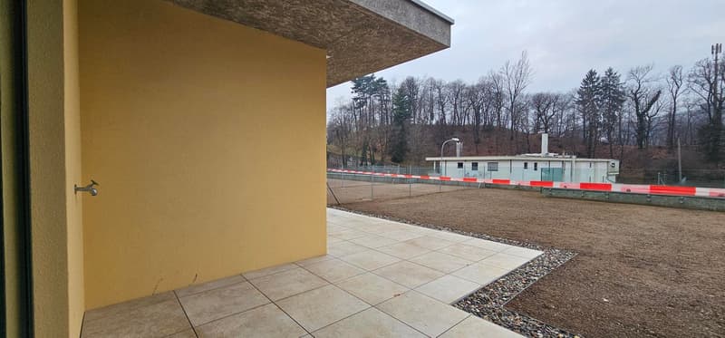 Yellow wall, tiled terrace, fenced area, trees, street light, building with windows in the distance