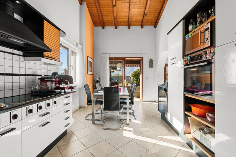 modern kitchen with white cabinets, black countertops, dining area with table and chairs, wooden ceiling, open door leading to balcony