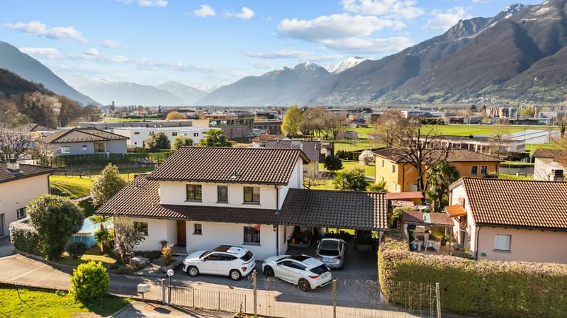 Detached house, brown roof, white walls, 3 cars parked in the garage, surrounded by greenery, mountains in the background