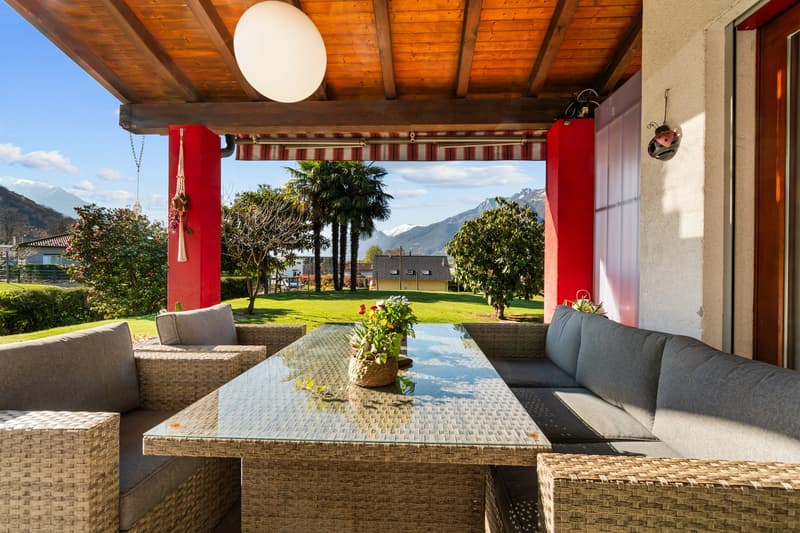 Outdoor seating area with a glass table, wicker couches, and a view of a grassy field and mountains