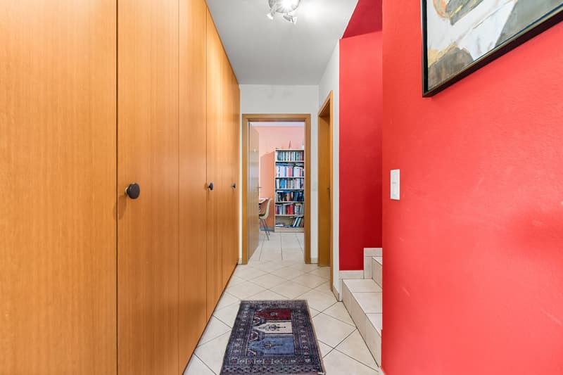 wooden cabinets, red wall, white tile floor, rug, bookshelf, picture frame
