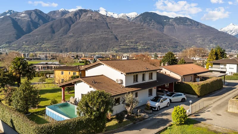Detached house, brown roof, white walls, swimming pool, 2 cars parked in front, green lawn, mountains in the background