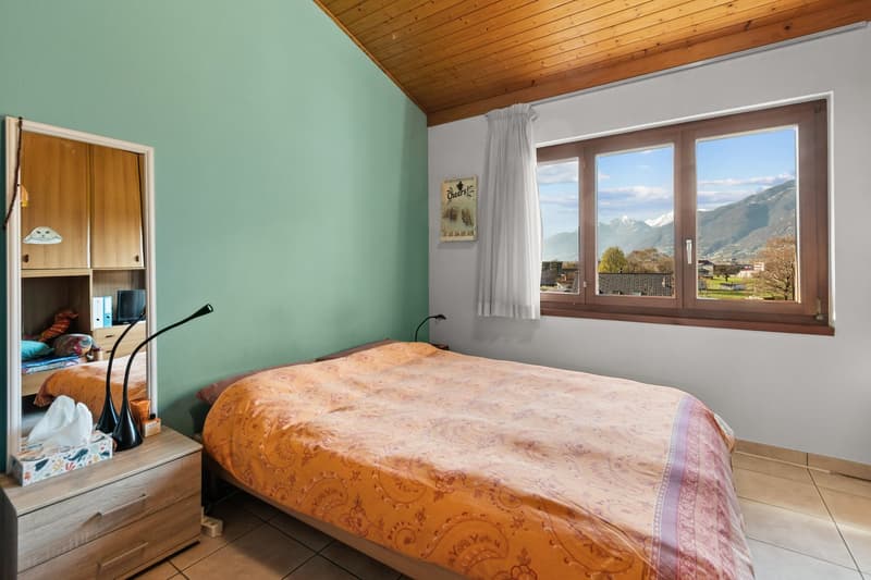bedroom with bed, nightstand, lamp, mirror, window with curtain, picture frame, and view of mountains