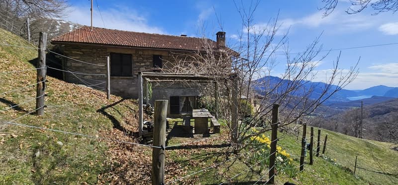 Stone house, red roof, chimney, wooden bench, surrounded by a fence, mountain view