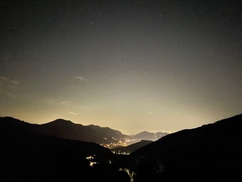Mountains under a starry night sky with city lights in the distance