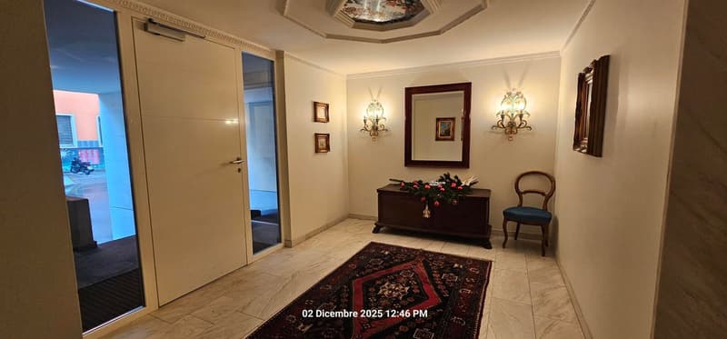 Entrance hallway with white walls, a mirror, a wooden chest, a chair, a rug, a decorative table, framed pictures, and decorative lamps.