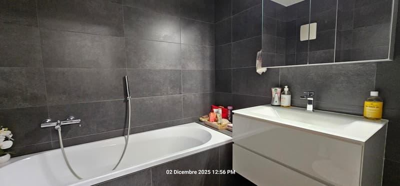 modern bathroom with bathtub, white vanity, mirror, and tiled walls