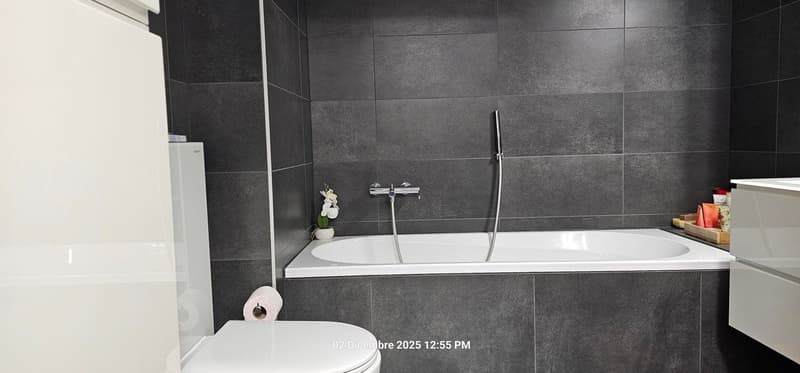 Bathroom with a bathtub, shower head, sink, toilet, white flooring, black tiles