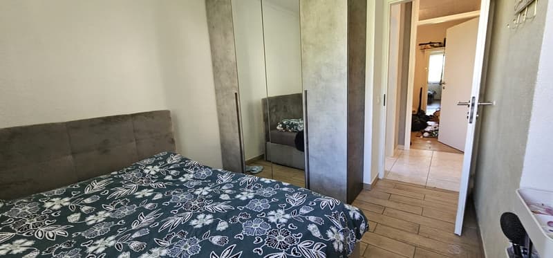 Bedroom with bed, large mirror, wooden floor, and a door leading to another room