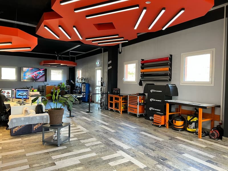 Wooden floor, red hanging lights, monitors, desk, cabinets, storage boxes, plant, tools, equipment, treadmill, windows