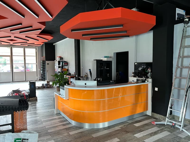 Orange reception counter, modern office setup, hanging lamps, wooden floor, large windows, potted plant, ladder against the wall