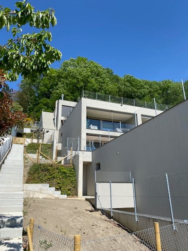 Modern multi-story house with balconies, surrounded by lush greenery and trees