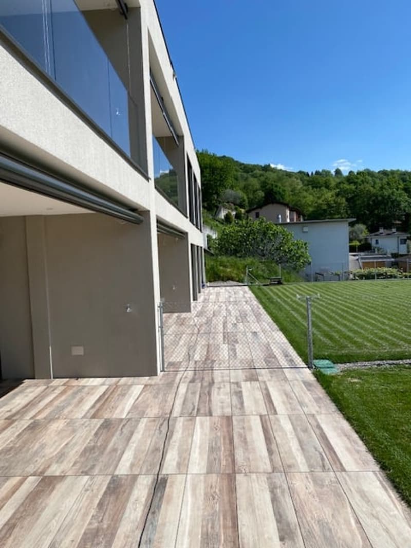 2-story modern house with large windows, wooden deck, and landscaped yard with grass and trees