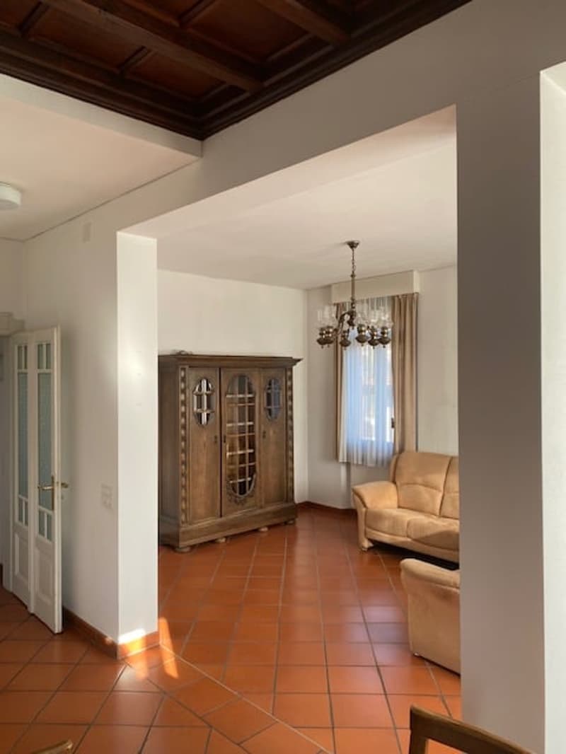 Open living room, beige couch, wooden cabinet, chandelier, tiled floor