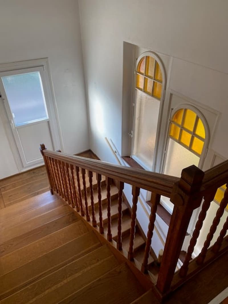 staircase with wooden handrail, wooden steps, white walls, wooden floor, two windows