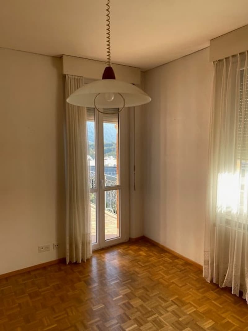 wooden floor, white walls, large glass door leading to balcony, white curtains, lamp