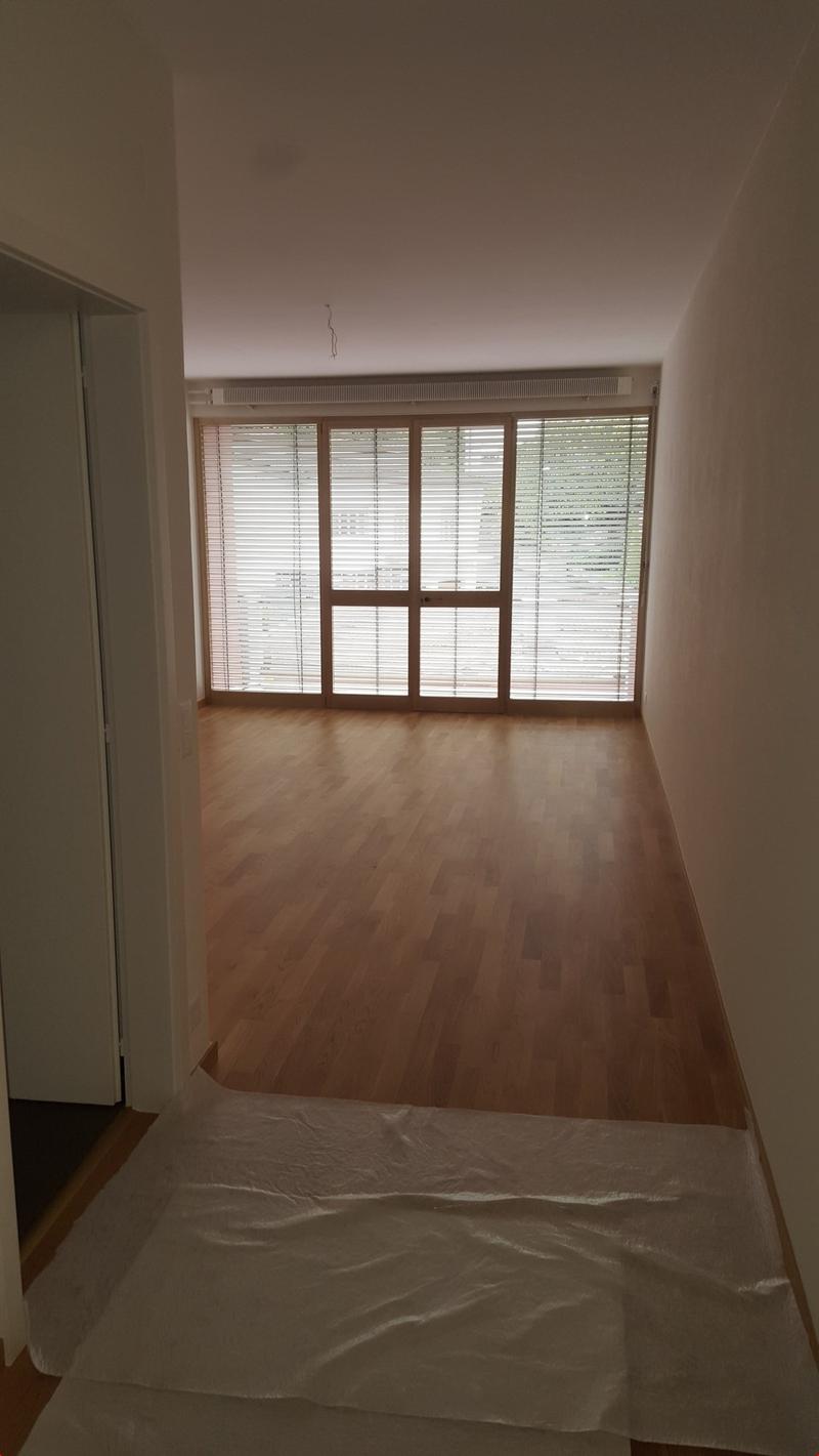 Empty room with wooden floors, white walls, large glass windows, and white tarpaulin on the floor.