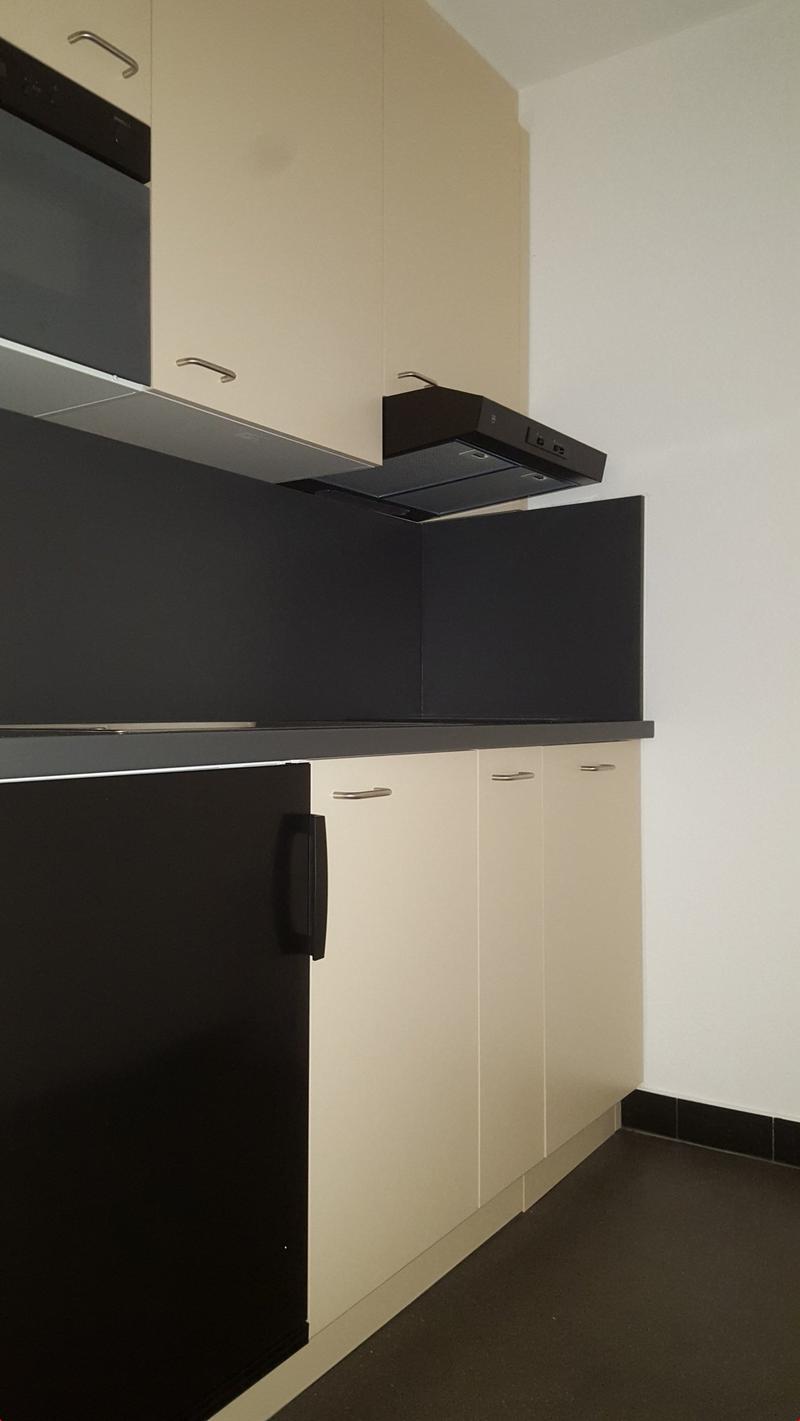 Modern kitchen with black countertops, beige cabinets, built-in oven and hood, large fridge, white walls, black flooring