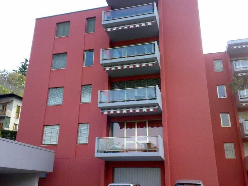 Red multi-story building with balconies, large windows, 2 cars parked in front