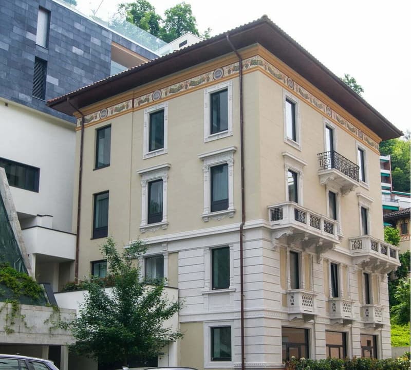3-story building, cream-colored facade, decorative white trim, glass windows, balconies, trees, greenery