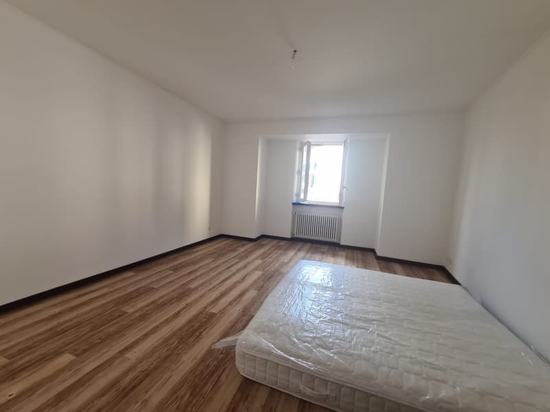 Empty room with wooden floor, white walls, window, radiator