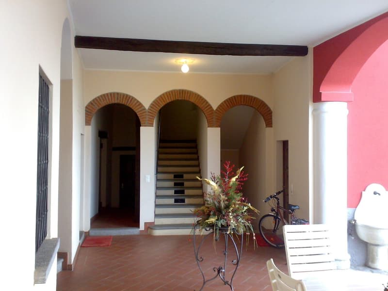 building entrance with arched passageways, red tiled floor, staircase, decorative plant, bicycles, chairs, white sink, lamp