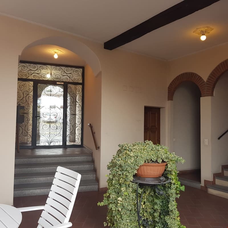 Entrance with staircase, arched doorways, decorative ceiling lamps, white exterior wall, greenery.