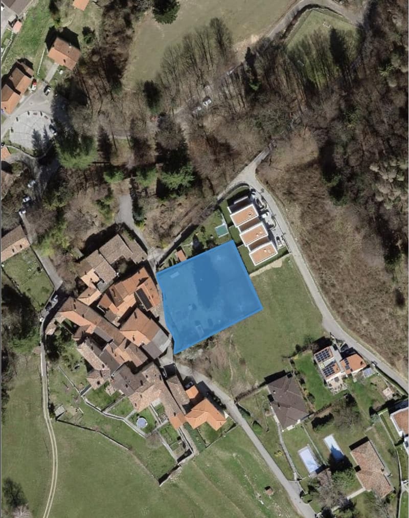 Aerial view of a cluster of buildings, highlighted blue area likely indicating a pool, surrounded by greenery and paths.