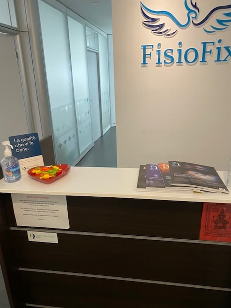 Reception desk with a white countertop, a blue sign, a red bowl of candies, a bottle of hand sanitizer, and some brochures