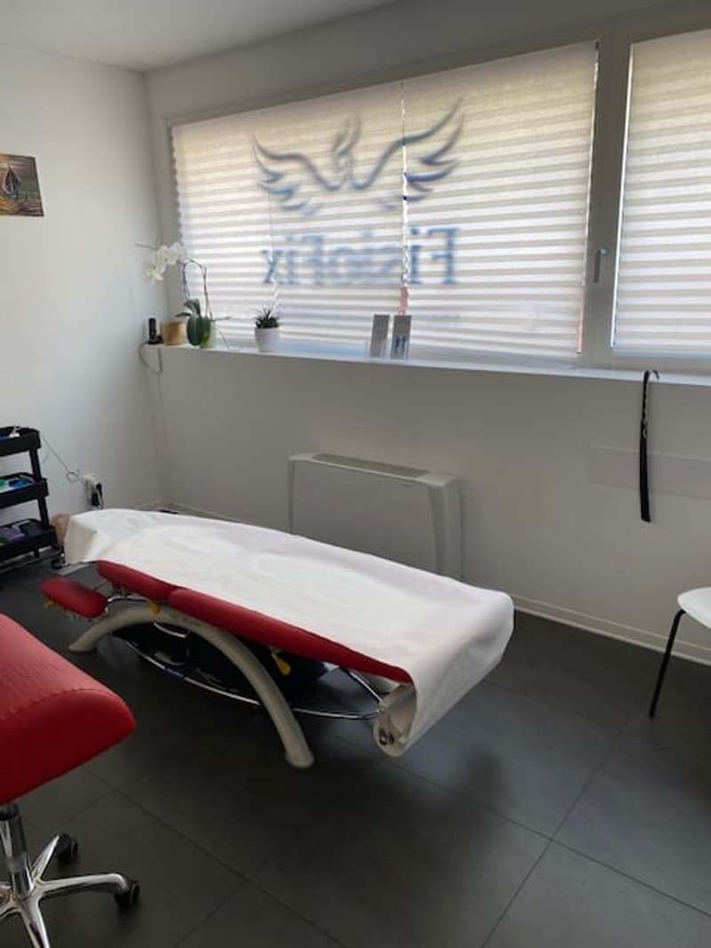 massage table, red chairs, white walls, white blinds, plants on window sill, radiator