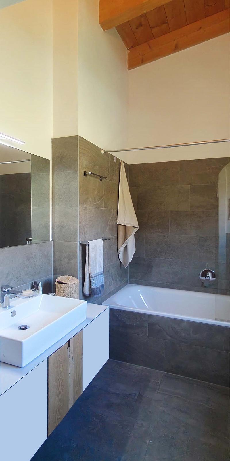 Bathroom with white sink, bathtub, wooden cabinet, mirror, towel rack, and tiled walls.