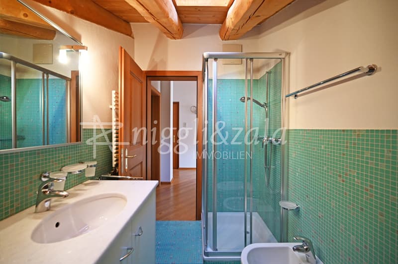 Bathroom with green tiles, white sink, mirror, shower, wooden floor, wooden beams