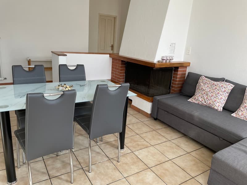 Dining area with a glass table, four chairs, a couch with pillows, and a fireplace