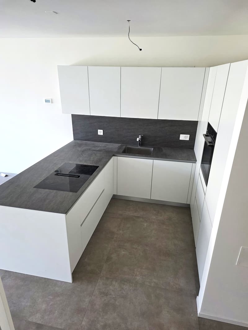 Modern kitchen with gray countertop, white cabinets, induction cooktop, and white ceramic floor